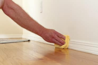 a person hand-cleaning the baseboard molding in their home