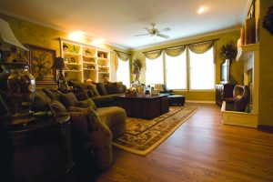 Cozy living room featuring hardwood flooring, light-colored walls, large windows with drapes, and a comfortable seating arrangement, highlighting current trends in wood flooring and interior design.