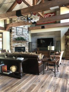 Rustic living room featuring wide, hand-scraped hardwood planks, exposed wooden beams, stone fireplace, and elegant furniture, reflecting current trends in hardwood flooring and interior design.
