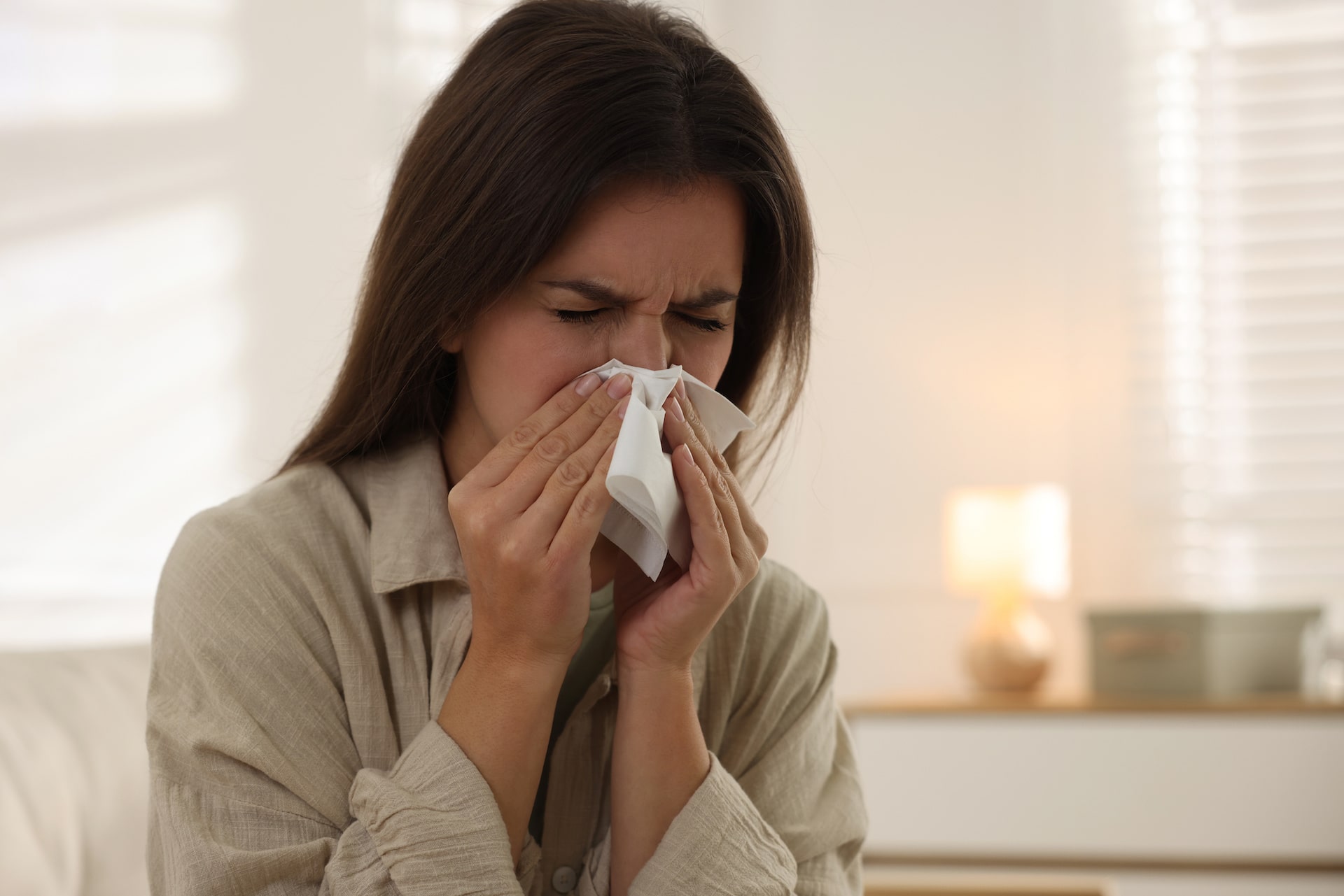 Woman sneezing into tissue in her home, possibly due to carpet allergens.