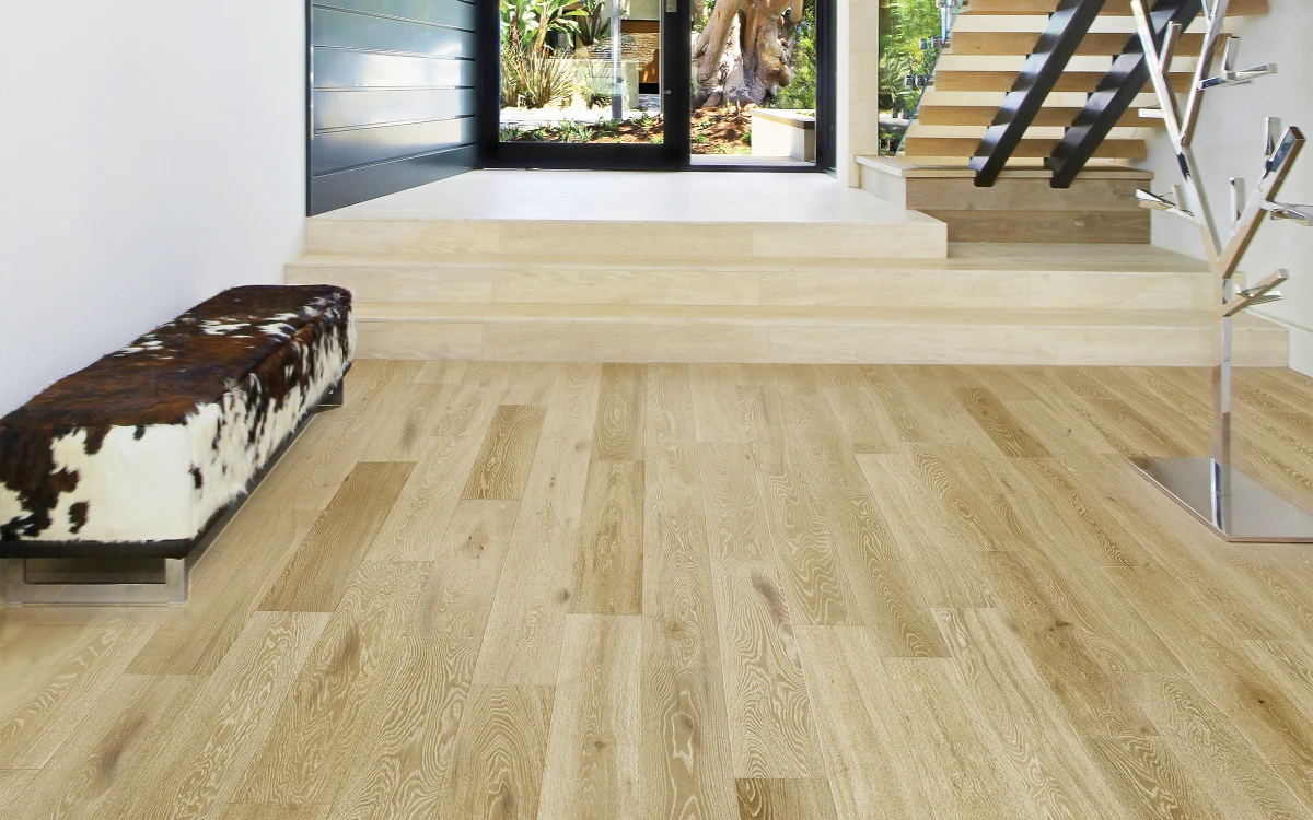 Naples hardwood flooring in a beach house setting, showcasing 6½" wide European Oak planks with warm tones and flowing grain patterns, complemented by a modern entryway with stairs and a decorative tree sculpture.
