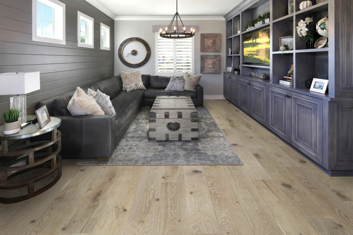 Living room featuring Coastal Fog hardwood flooring from the D&M Silver Oak Reserve Collection, with a modern black leather sectional sofa, decorative pillows, a rustic coffee table, and stylish decor elements.