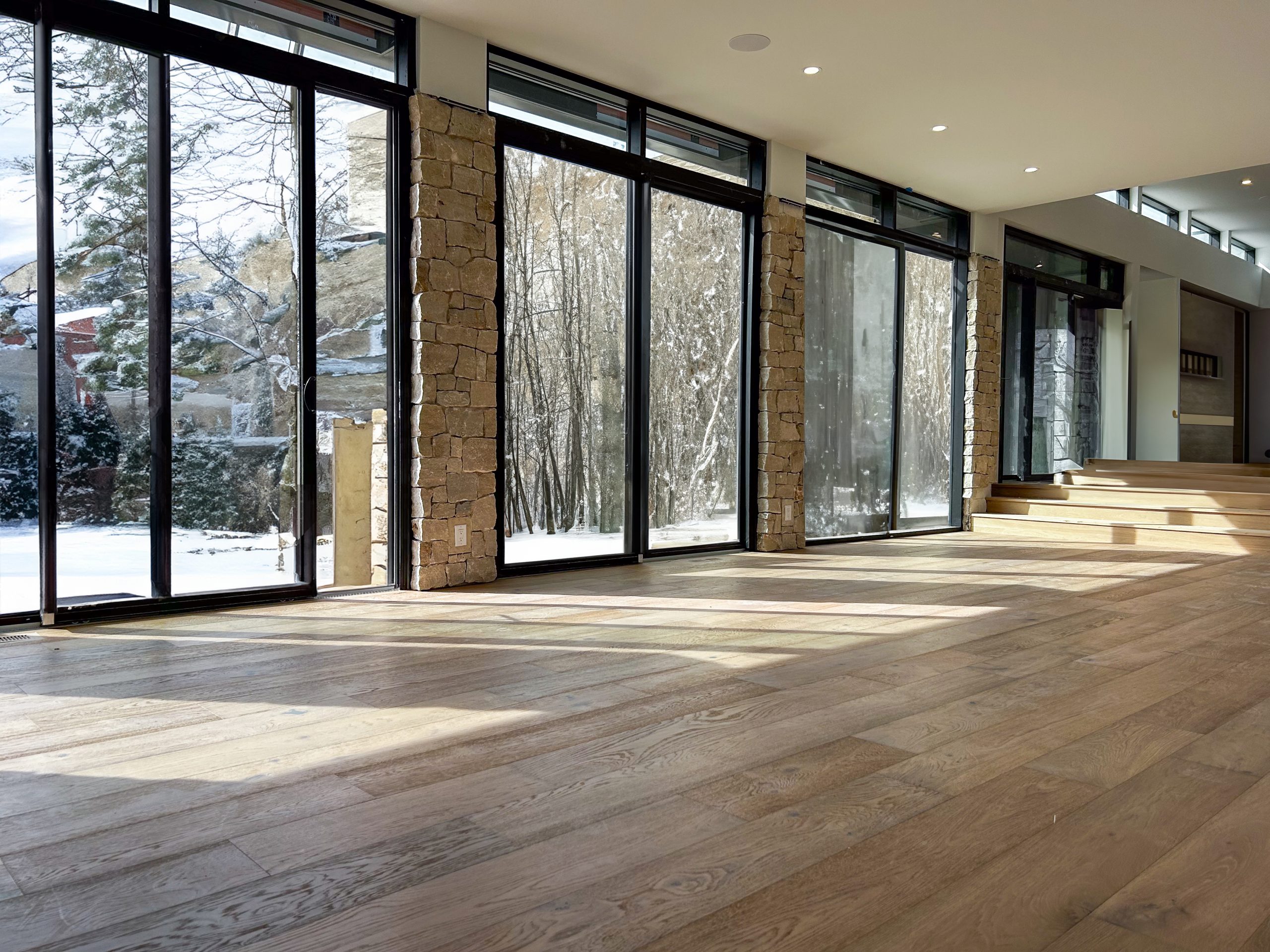 Spacious interior showcasing hardwood flooring from the Palms Collection, large windows revealing a snowy landscape, and natural light enhancing the warm tones of the wood.