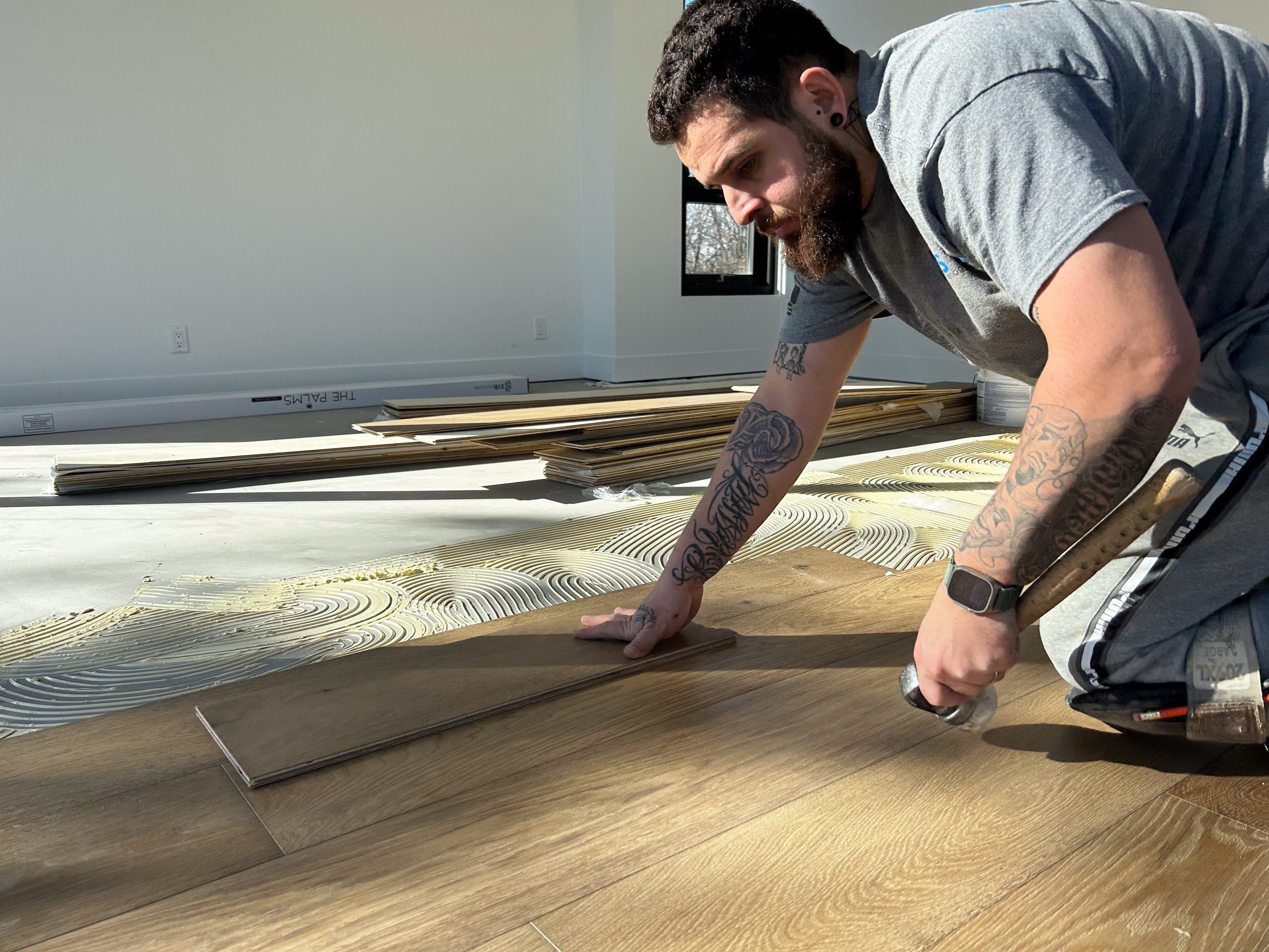 Man installing wide-plank Copacabana hardwood flooring from The Palms Collection in a modern interior, showcasing craftsmanship and durability.