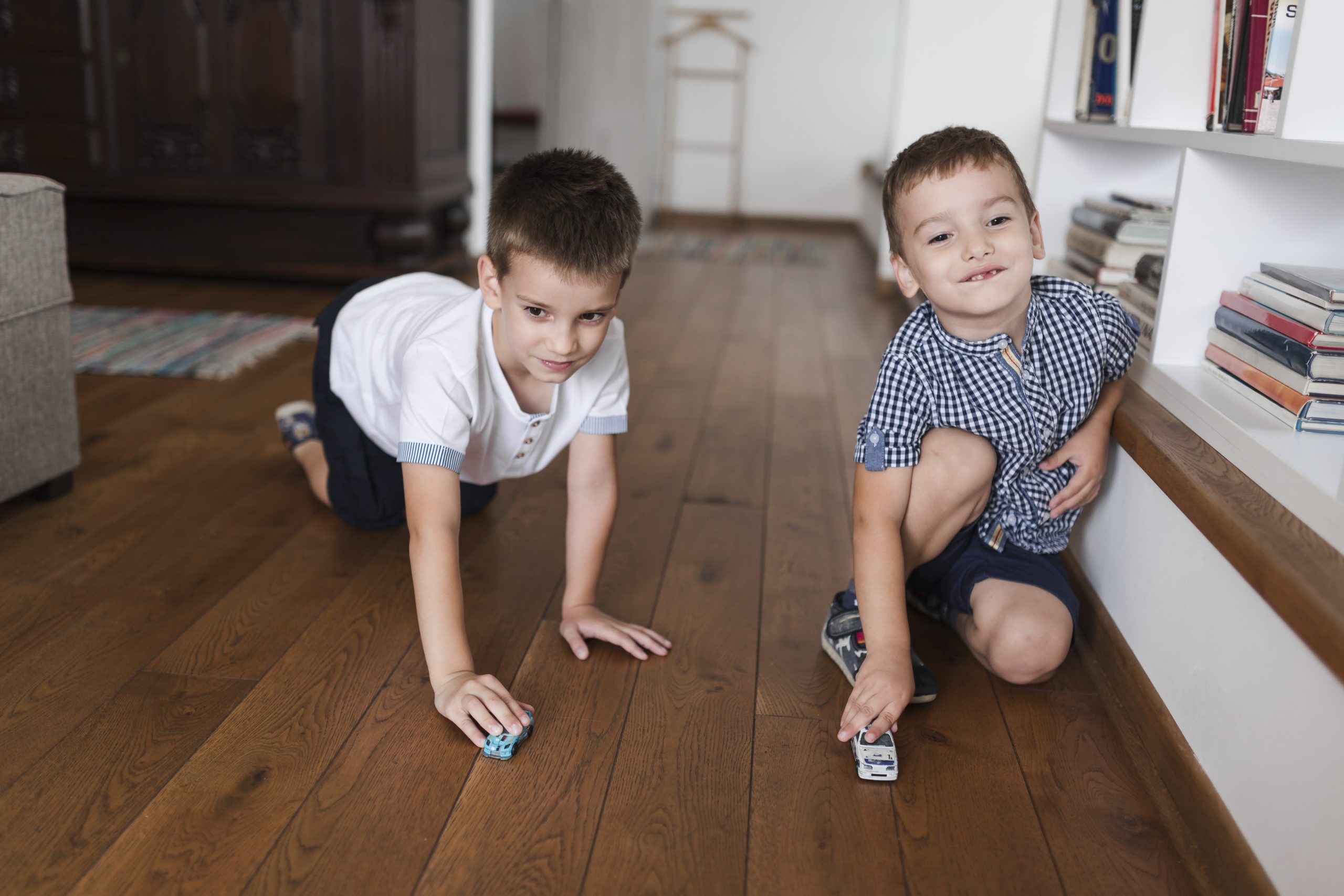Two young boys playing with toy cars on hardwood floor.